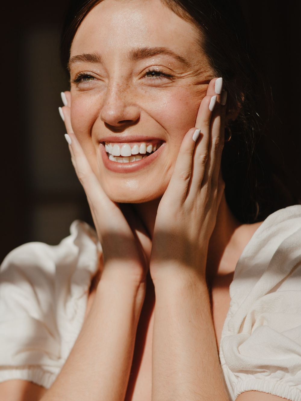 Mujer sonriendo con las manos en el rostro